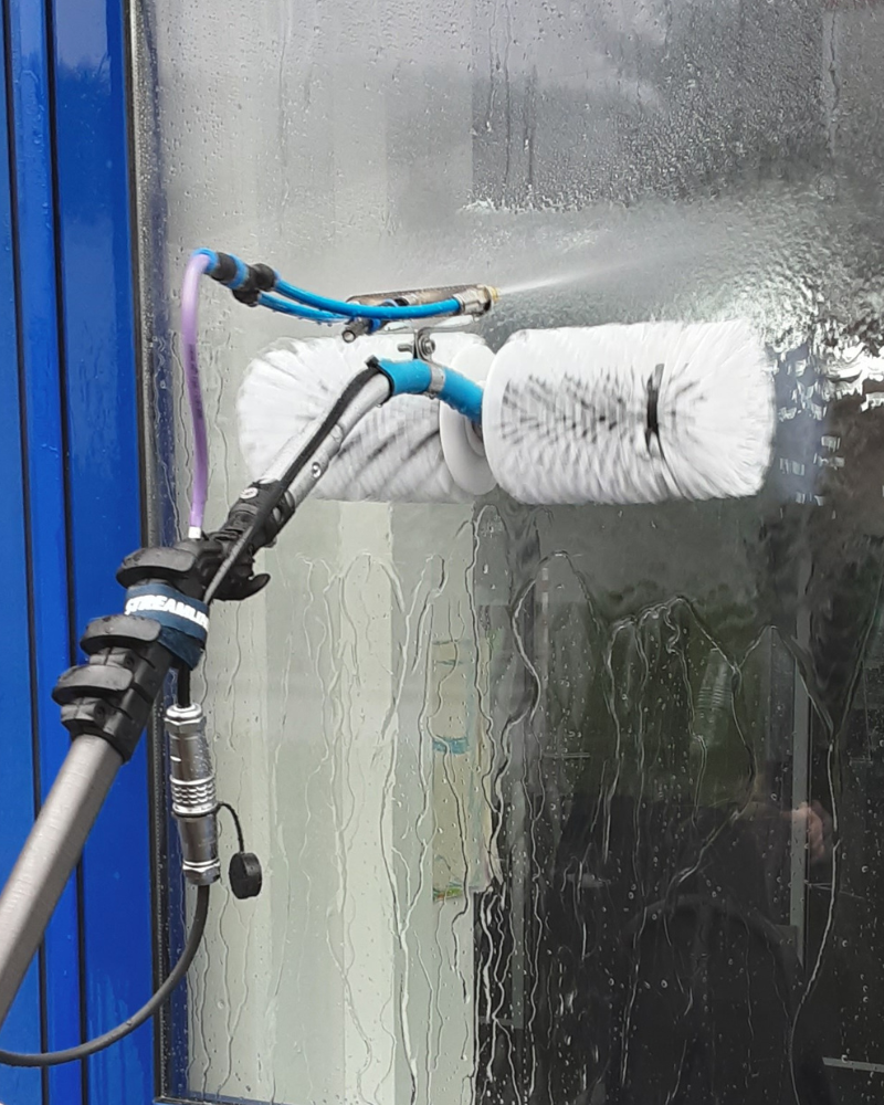 weisse, rotierende Bürste auf Fensterscheibe mit Wassersprüher